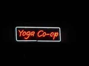 Red neon sign reading Yoga Co-op with white rectangular border against dark background