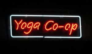 Red neon sign reading Yoga Co-op with white rectangular border glowing against dark background